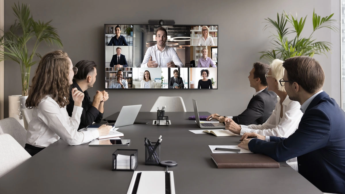 A diverse team in a conference room, actively involved in a video conference with colleagues joining remotely.